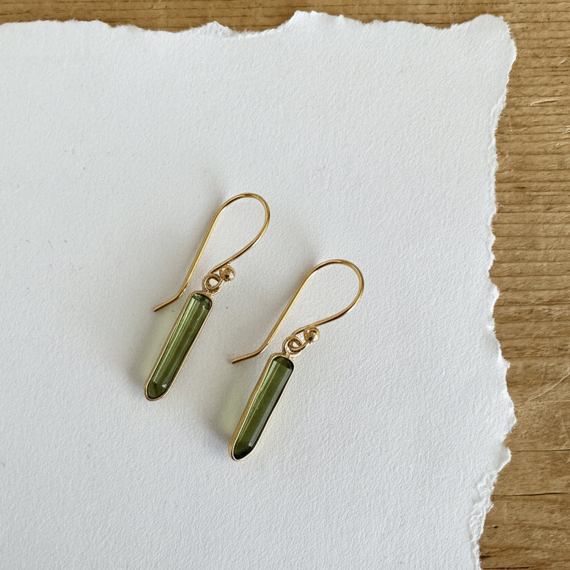 Gold tone earring featuring a green toned rectangular tourmaline gemstone dangling from a hook.