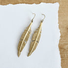 Gold toned feather hanging from a gold toned hook.