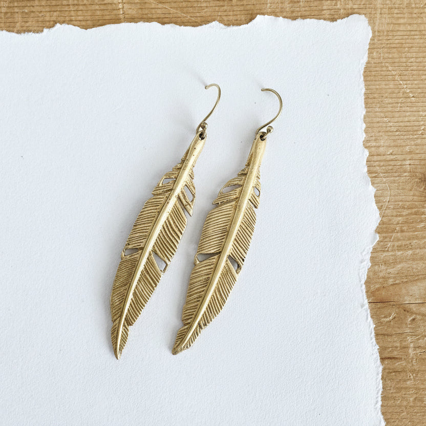 Gold toned feather hanging from a gold toned hook.