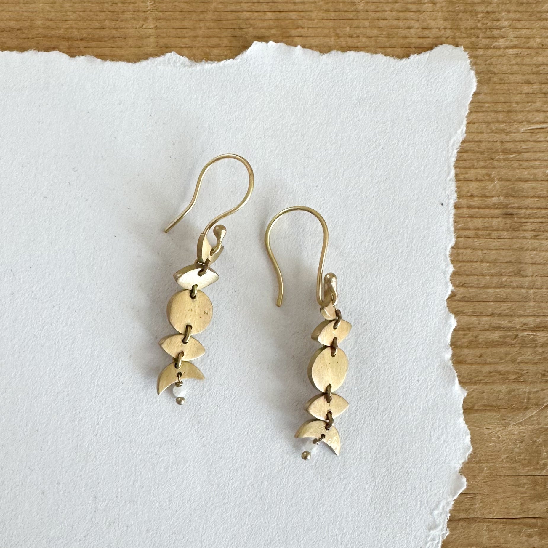 Gold toned earring featuring phases of the moon dangling from a hook.