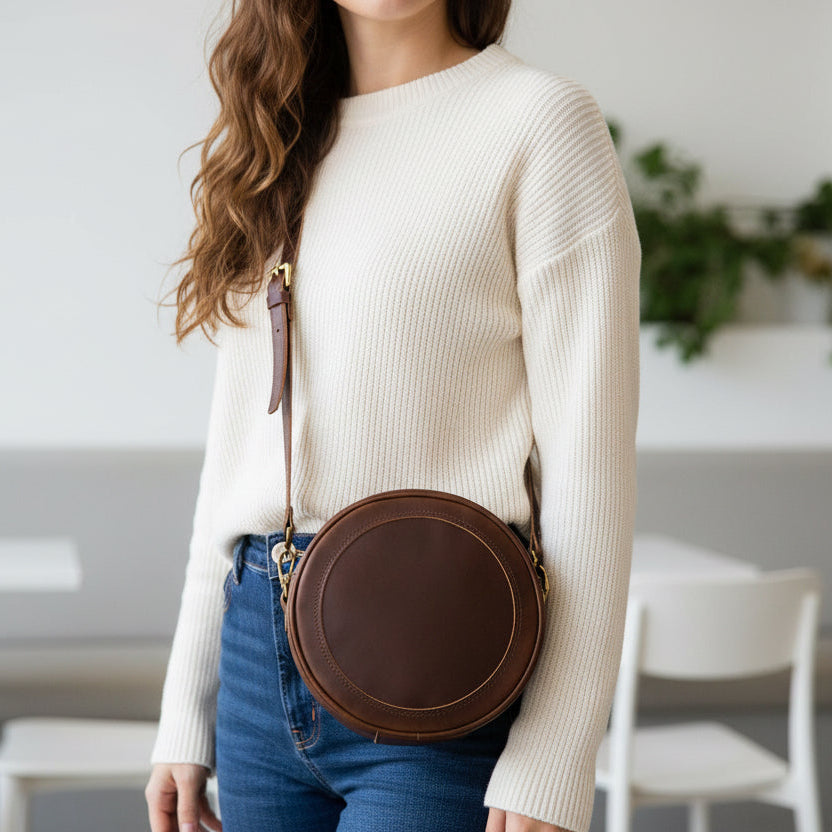 Deep brown circular cross body leather bag with antique brass hardware.