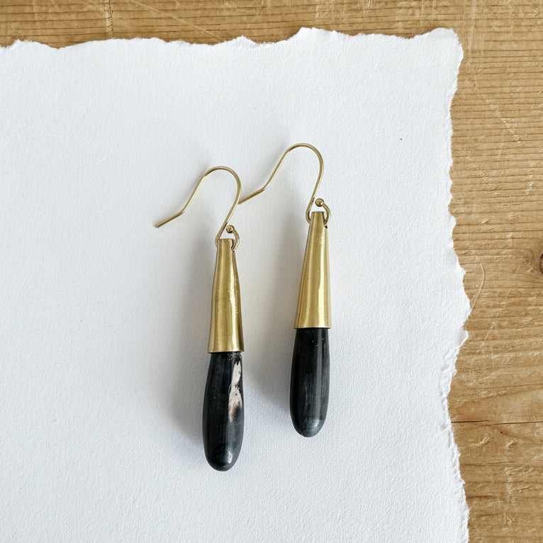 Dark horn partially surrounded in a gold tone cylinder hanging from a gold tone hook.