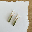 Gold tone earring featuring a green toned rectangular tourmaline gemstone dangling from a hook.